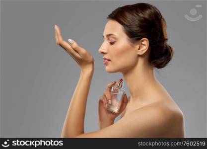 perfumery, beauty and luxury concept - happy young woman smelling perfume from her wrist over grey background. happy woman smelling perfume from her wrist