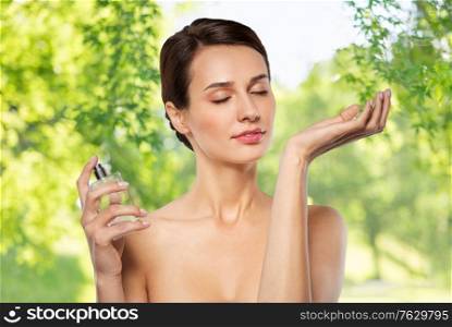 perfumery, beauty and luxury concept - happy young woman smelling perfume from her wrist over green natural background. happy woman smelling perfume from her wrist