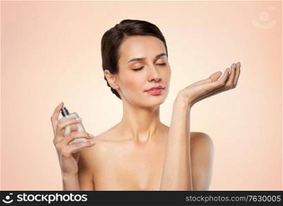 perfumery, beauty and luxury concept - happy young woman smelling perfume from her wrist over beige background. happy woman smelling perfume from her wrist