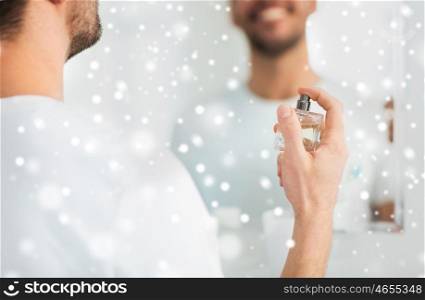 perfumery, beauty and people concept - close up of happy smiling young man with perfume looking to mirror using scent at bathroom over snow