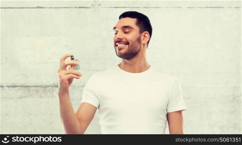 perfumery, beauty and people concept - happy smiling young man with male perfume over gray stone wall background. smiling man with male perfume over gray background