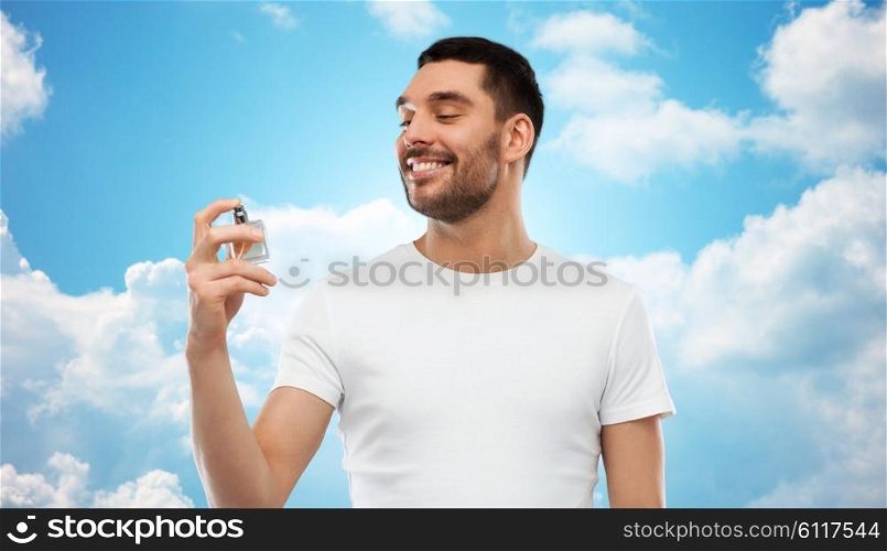 perfumery, beauty and people concept - happy smiling young man with male perfume over blue sky and clouds background