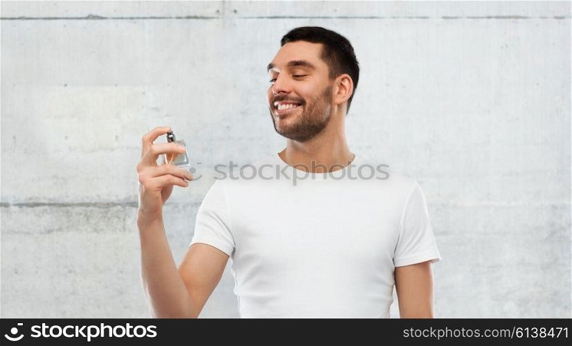 perfumery, beauty and people concept - happy smiling young man with male perfume over gray stone wall background