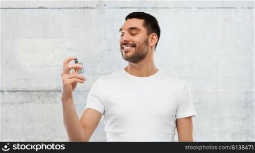 perfumery, beauty and people concept - happy smiling young man with male perfume over gray stone wall background