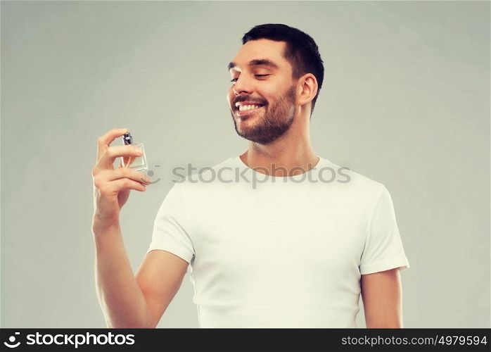 perfumery, beauty and people concept - happy smiling young man with male perfume over gray background. smiling man with male perfume over gray background