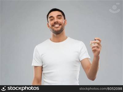 perfumery, beauty and people concept - happy smiling young man with male perfume over gray background