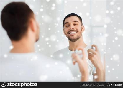 perfumery, beauty and people concept - happy smiling young man with perfume looking to mirror using scent at bathroom over snow