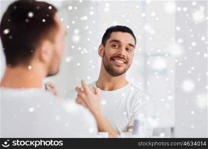 perfumery, beauty and people concept - happy smiling young man with perfume looking to mirror using scent at bathroom over snow