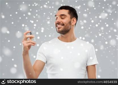 perfumery, beauty, winter, christmas and people concept - happy smiling young man with male perfume over snow on gray background