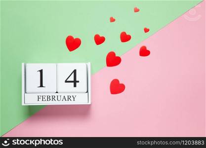 Perpetual calendar with date of February 14, red different-sized confetti hearts on two-color background pink and green. Flat lay. Top view. St. Valentine?s Day celebration concept. Horizontal.