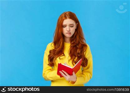 Perplexed and uneasy, concerned cute redhead female student having troubles with schedule, frowning reading girlfriend diary, feeling guilty, holding red notebook, feeling troubled, blue background.. Perplexed and uneasy, concerned cute redhead female student having troubles with schedule, frowning reading girlfriend diary, feeling guilty, holding red notebook, feeling troubled, blue background