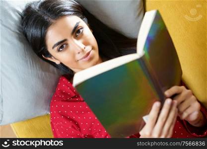 Persian woman at home reading on a couch wearing pyjamas. Persian woman at home reading on a couch