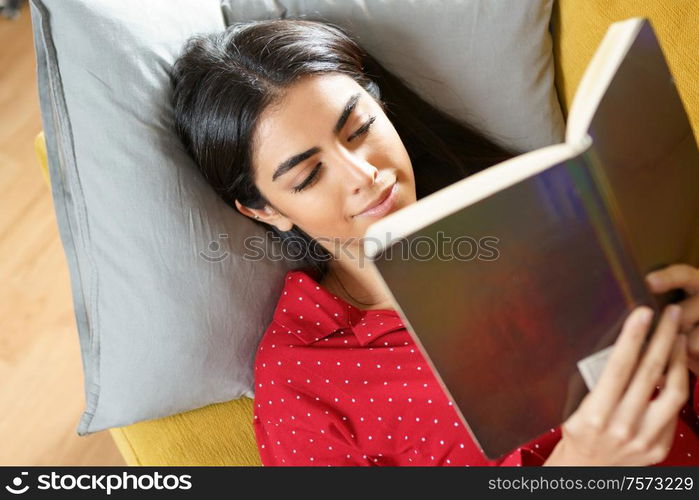 Persian woman at home reading on a couch wearing pyjamas. Persian woman at home reading on a couch