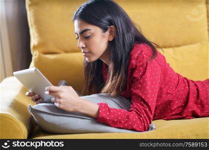 Persian woman at home using digital tablet on a couch. Persian woman at home using digital tablet