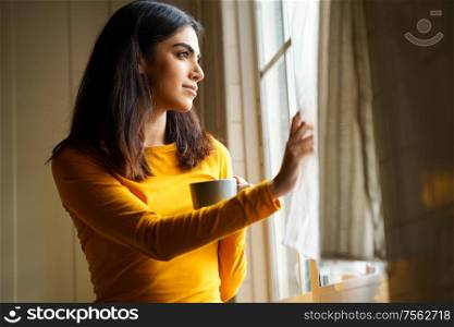 Persian woman drinking coffee at home while looking through the window. Persian woman drinking coffee while looking through the window