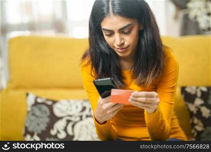 Persian woman shopping online with her smartphone, paying with her credit card. Woman shopping with smartphone paying with her credit card