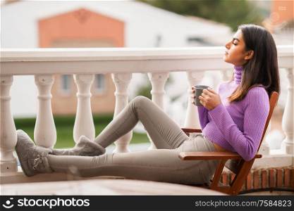 Persian woman sitting in an armchair on her balcony having a mug of coffee. Persian woman on her balcony having a mug of coffee