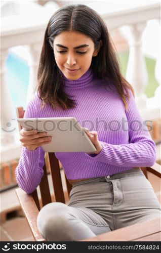 Persian woman sitting in an armchair on her balcony using digital tablet. Persian woman on her balcony using digital tablet