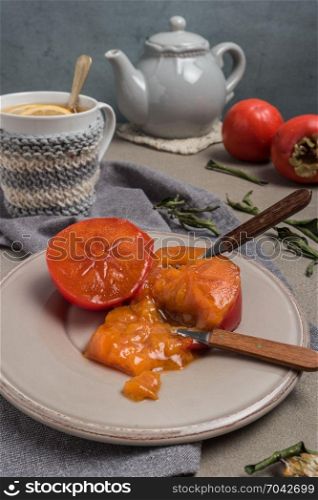 Persimmon fruit on the plate and lemon tea. Rustic background in vintage style