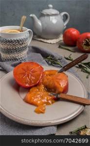 Persimmon fruit on the plate and lemon tea. Rustic background in vintage style
