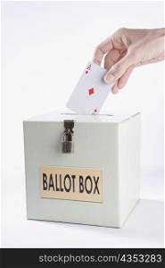 Person&acute;s hand inserting a playing card into a ballot box