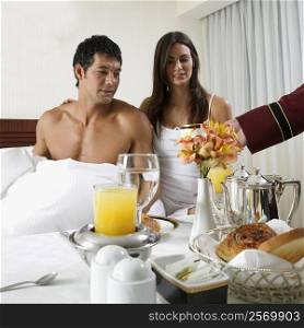 Person&acute;s hand serving tea to a young woman and a mid adult man on the bed