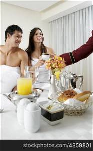 Person&acute;s hand serving tea to a young woman and a mid adult man on the bed