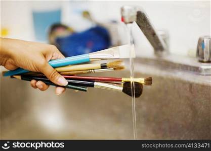 Person&acute;s hand washing paint brushes under a faucet