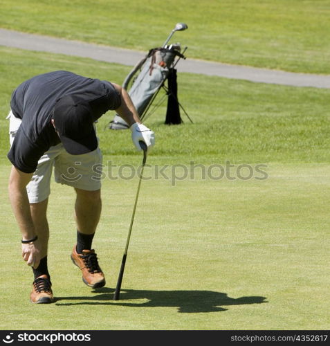 Person bending holding a golf ball and a golf club