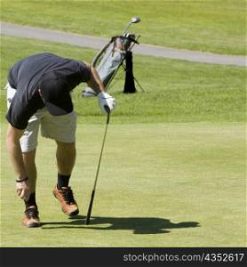 Person bending holding a golf ball and a golf club