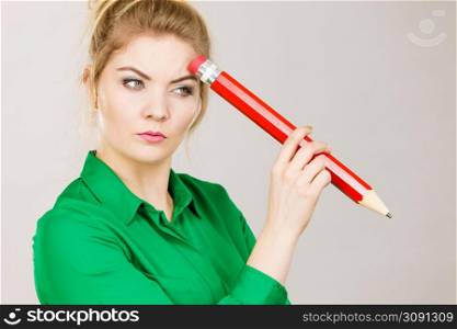 Person confused thinking seeks a solution. Pensive thoughtful student girl or business woman female teacher coming up with an idea, holding big red pencil. Studio shot on grey.. Woman confused thinking, big pencil in hand
