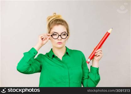 Person confused thinking seeks a solution. Pensive thoughtful student girl or business woman female teacher coming up with an idea, holding big red pencil. Studio shot on grey.. Woman confused thinking, big pencil in hand
