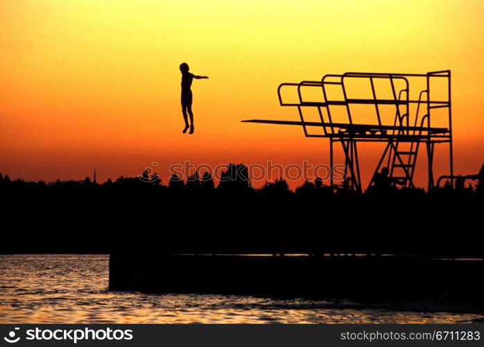 Person diving off a diving board while the sun sets