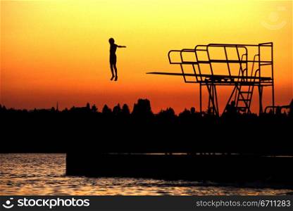 Person diving off a diving board while the sun sets