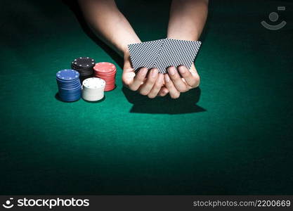 person hand holding playing card with stacking poker chips casino table