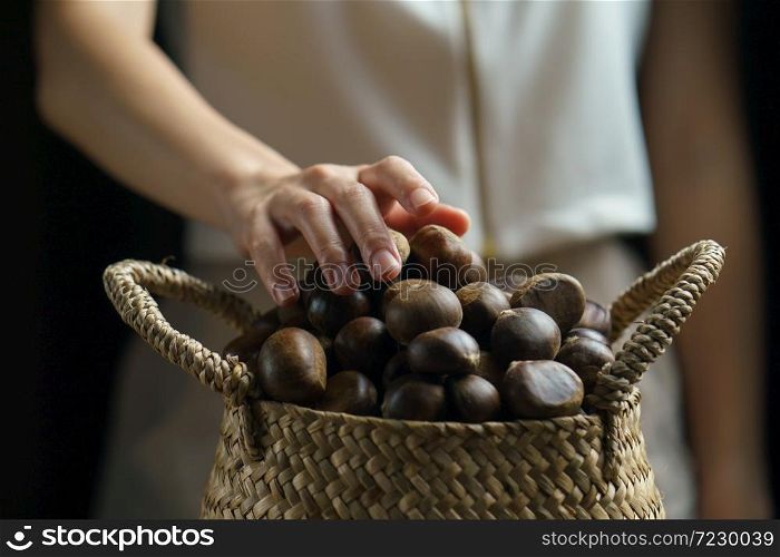Person holding chestnuts on hand with wicker basket full of chestnuts.
