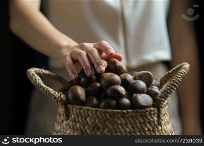 Person holding chestnuts on hand with wicker basket full of chestnuts.
