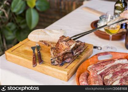 person holding fresh grilled beef steak with tong wooden board