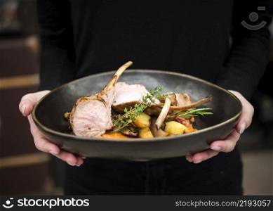 person holding lamb ribs dish