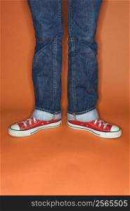 Person in jeans and sneakers with feet turned outward.