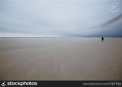 Person in the middle of wide sandy beach landscape against overcast sky on moody day at North Sea, Amrum, Norddorf, Germany, Schleswig-Holstein