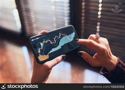 Person investing trading on stock cryptocurrency market using investing application on smartphone. Stock market investment in hand. Trader holding mobile phone looking at candle chart