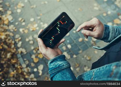Person investing trading on stock cryptocurrency market using investing application on smartphone. Stock market investment in hand. Trader holding mobile phone looking at candle chart. Man investing trading on stock cryptocurrency market using investing application on smartphone. Stock market investment in hand. Trader holding mobile phone looking at candle chart