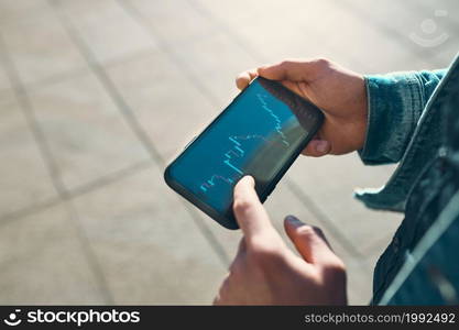 Person investing trading on stock cryptocurrency market using investing application on smartphone. Stock market investment in hand. Trader holding mobile phone looking at candle chart. Man investing trading on stock cryptocurrency market using investing application on smartphone. Stock market investment in hand. Trader holding mobile phone looking at candle chart