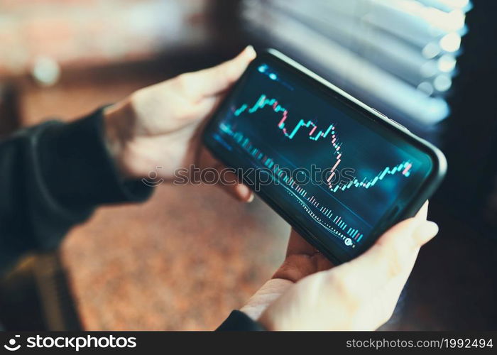 Person investing trading on stock cryptocurrency market using investing application on smartphone. Stock market investment in hand. Trader holding mobile phone looking at candle chart