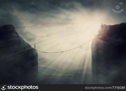 Person on the edge of precipice determined to overcome the obstacle by passing an old slackline bridge. The pursuit of success, danger and risk concept. Tightrope between two peaks, metaphoric scene