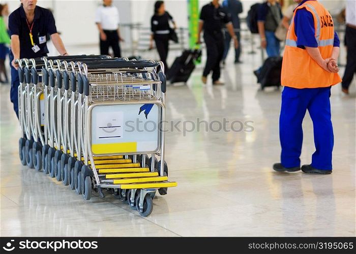 Person pushing a row of luggage carts at an airport, Madrid, Spain