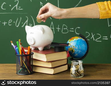 person putting coins piggy bank with books pencils