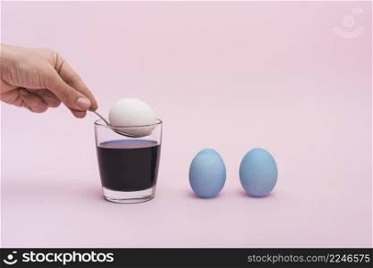 person putting spoon with egg into glass with paint