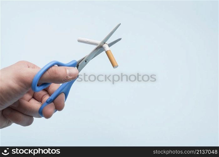 person s hand broking cigarette with scissor blue background